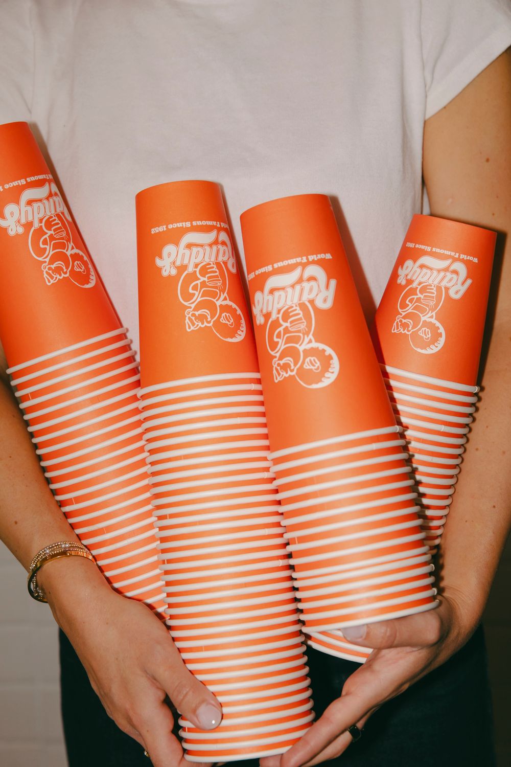 Stacks of branded orange Randy's Donuts cups held in both arms