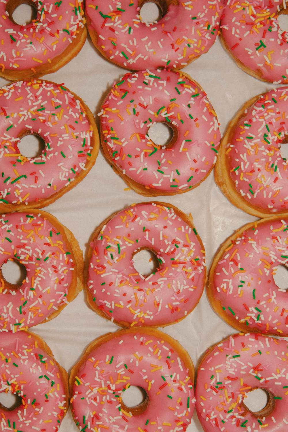 Overhead view of pink sprinkle donuts laid out in a grid