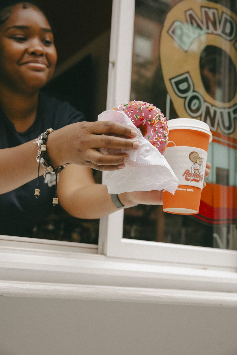 A Randy's Donuts team member handing a sprinkled donut and a coffee through the shop window
